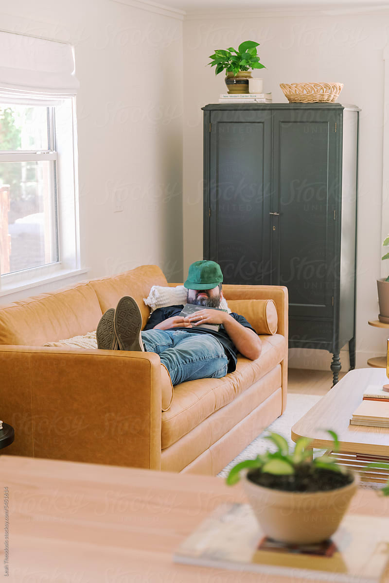 Millennial bearded Man sleeping on sofa with hat over face and feet up