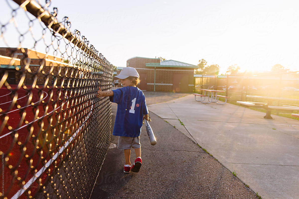 little boy walks down path after a bace-ball game.