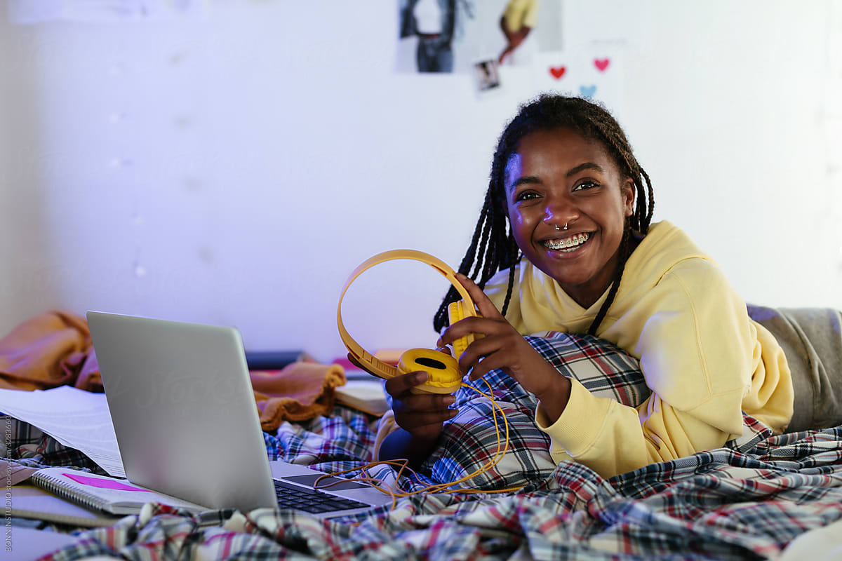 Cheerful African American teenager with headphones on bed