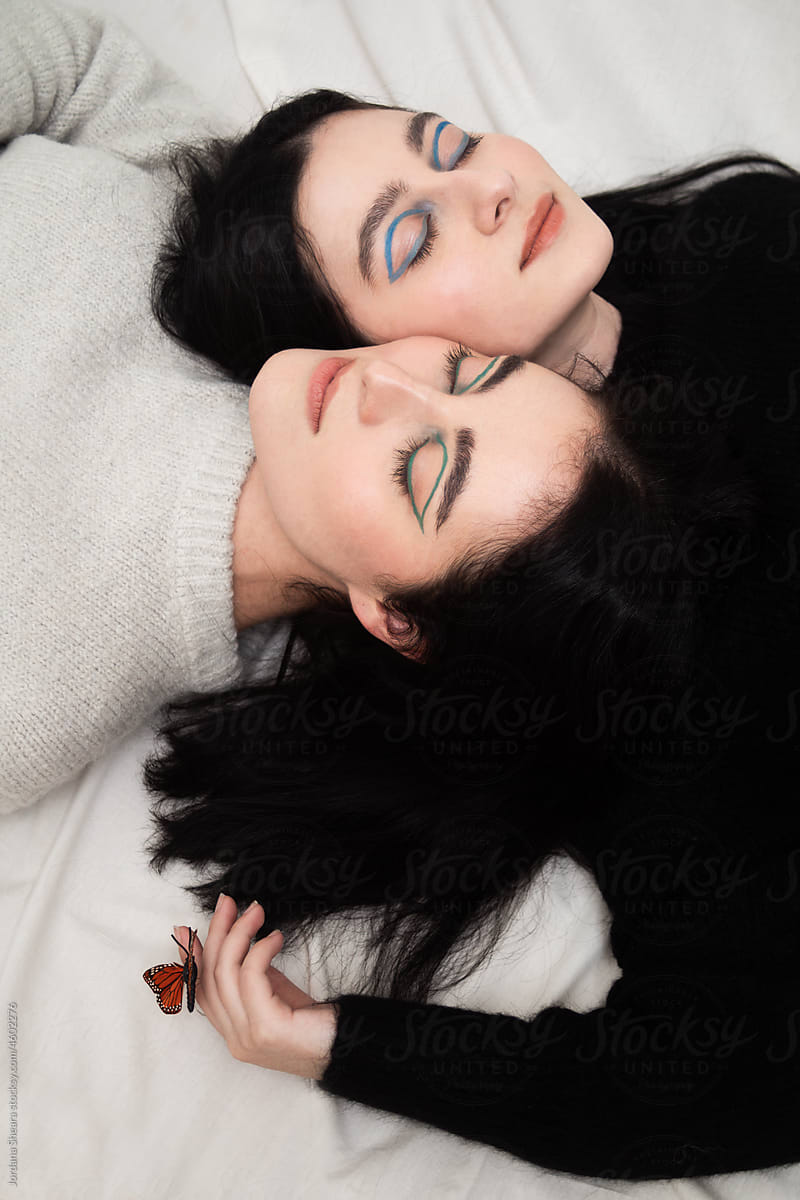 twin sisters laying shoulder to shoulder on white backdrop