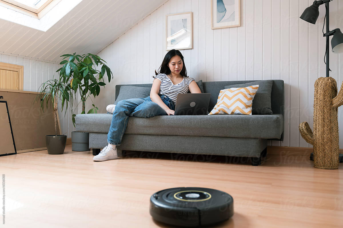 Young woman working on laptop with robot vacuum cleaner
