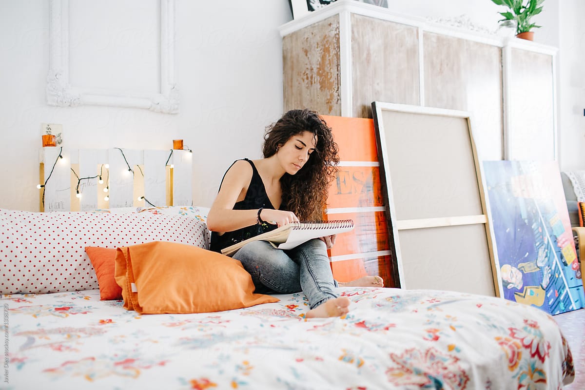 Young woman sitting on bed and drawing