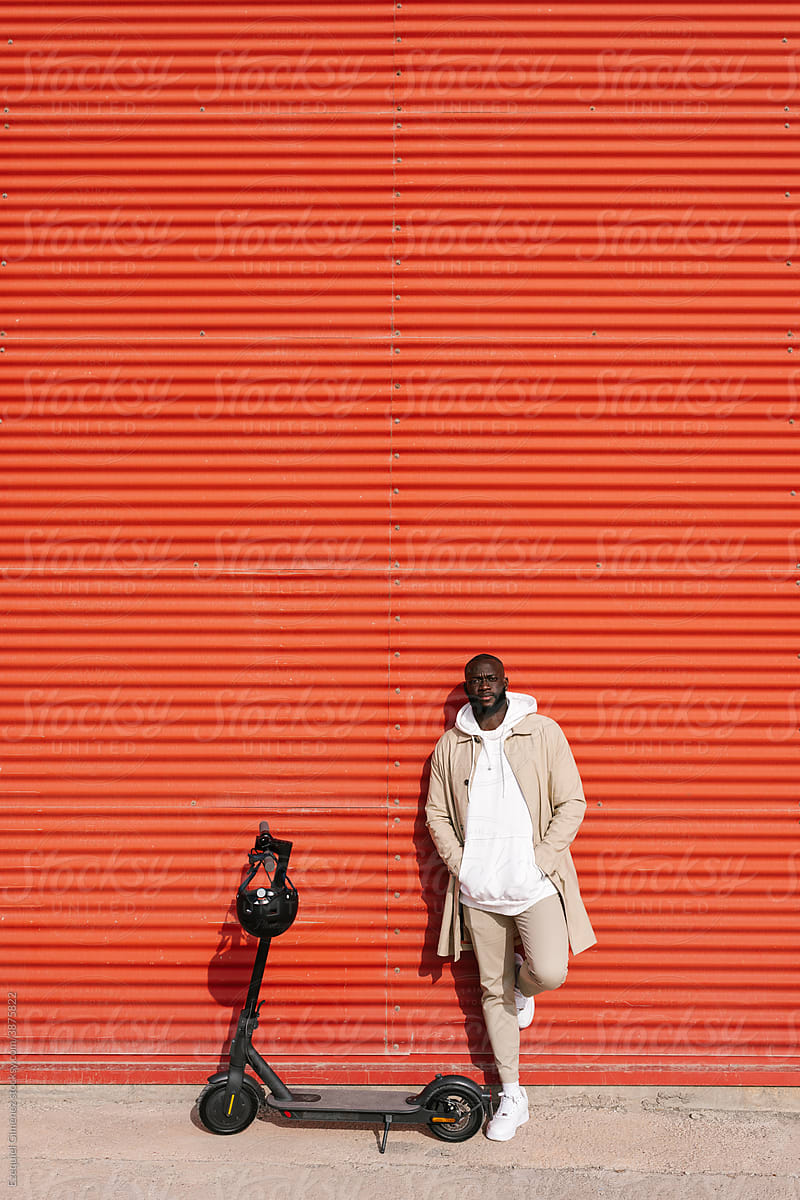 Black man leaning on a wall with an electric scooter