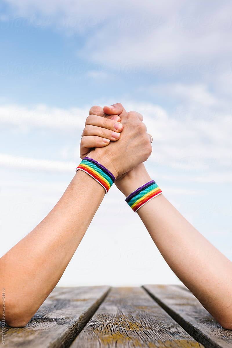 Unrecognizable persons holding hands with gay flag bracelets in arm wrestling challenge