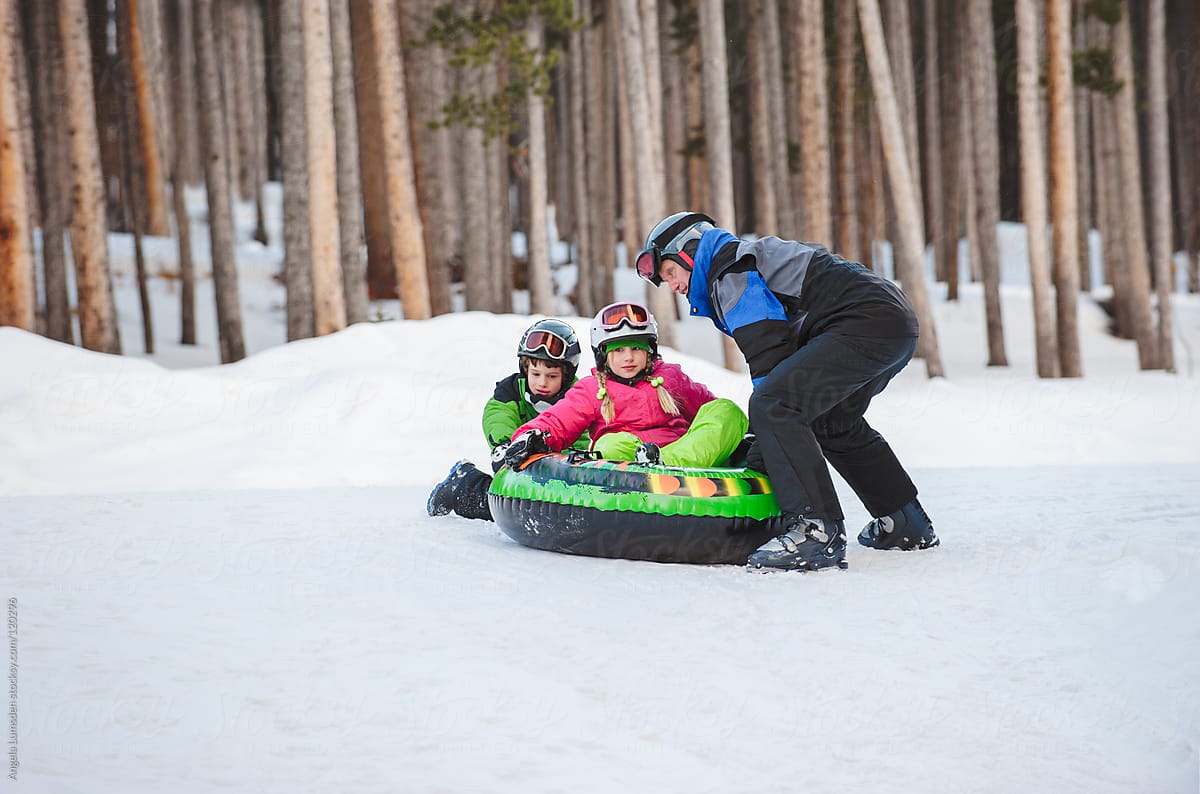 Father and two children playing with a toboggan in winter