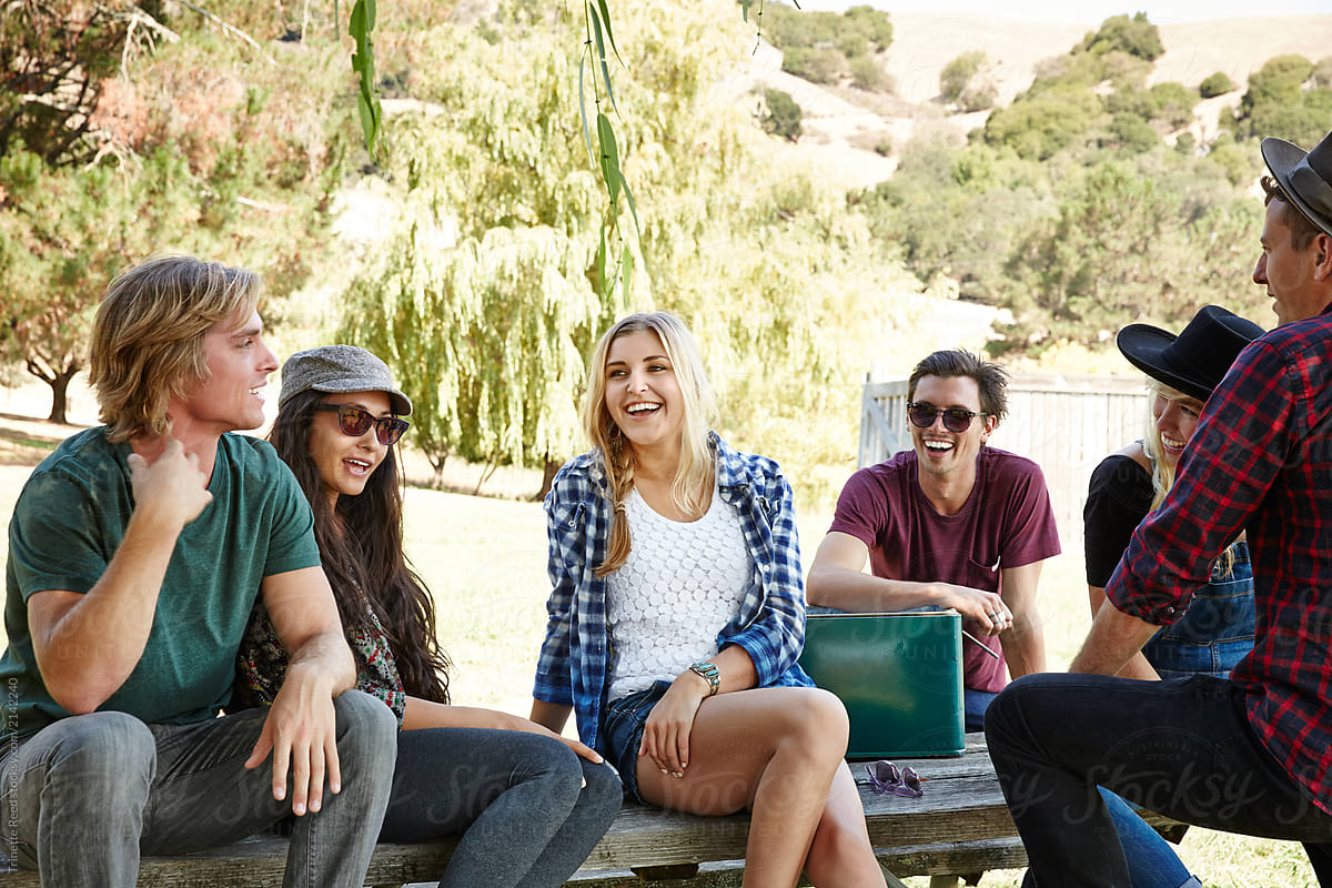 Group of Millennial friends hanging out on picnic table in park