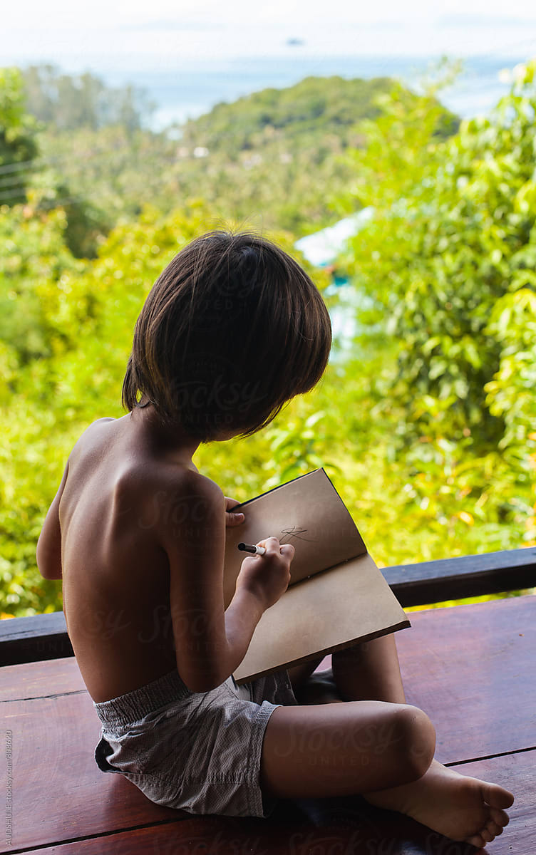 Small boy learning/writing his homework  in the middle of the jungle.