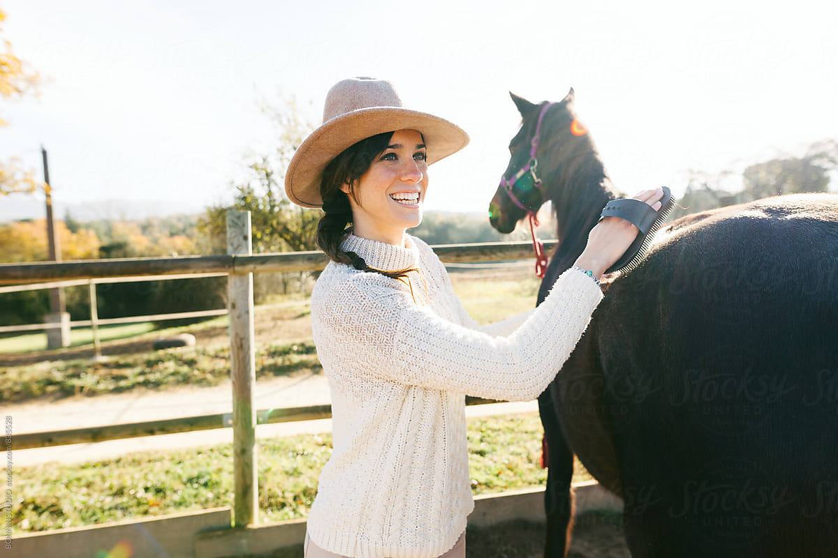 Happy woman brushing her horse in a ranch.