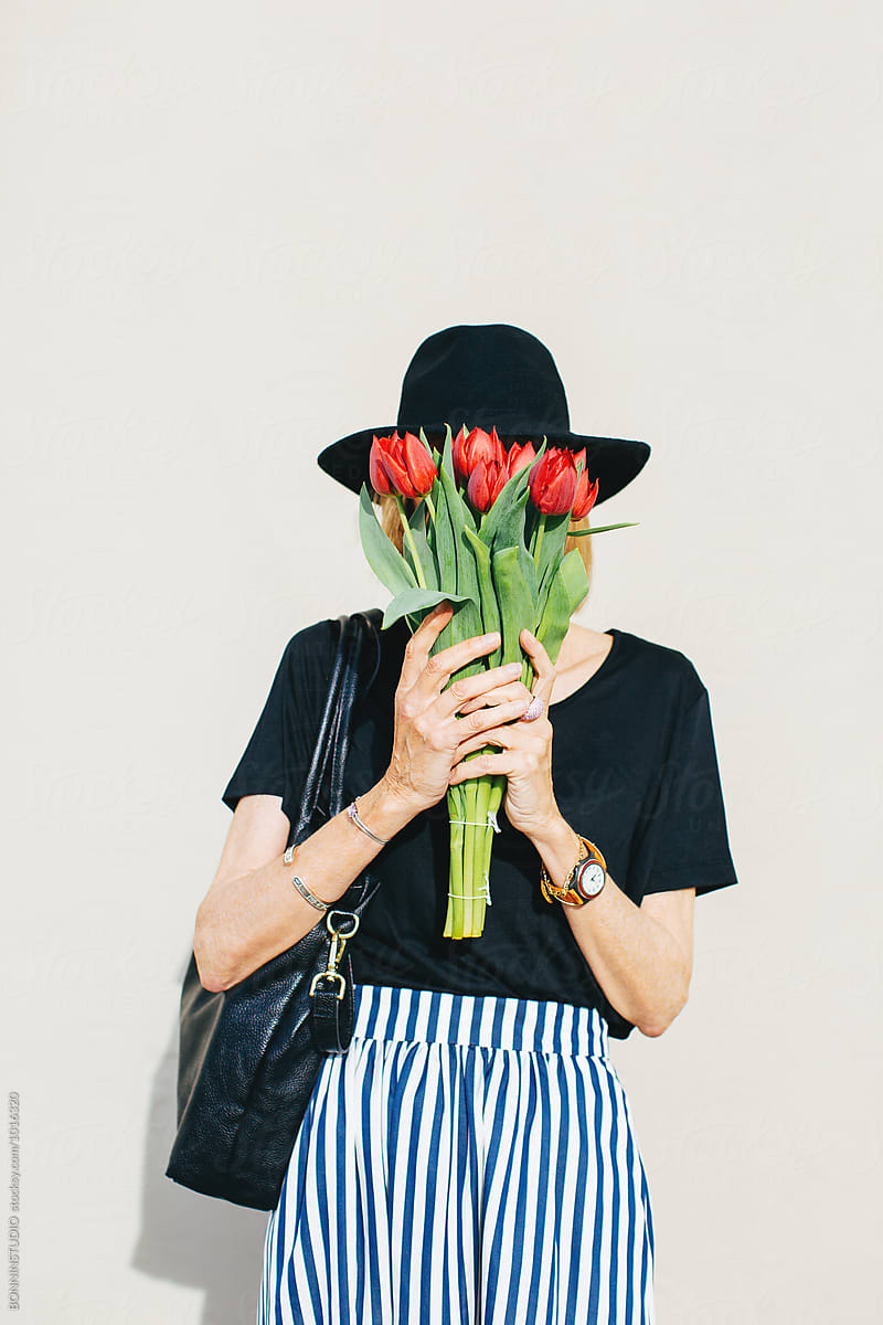 Stylish senior woman hiding her face with a bouquet of red tulips outside.