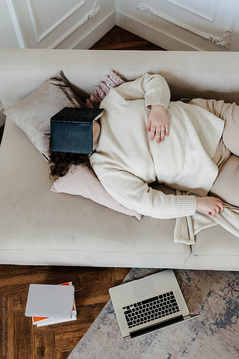 Anonymous lady lying on sofa with notebook on face