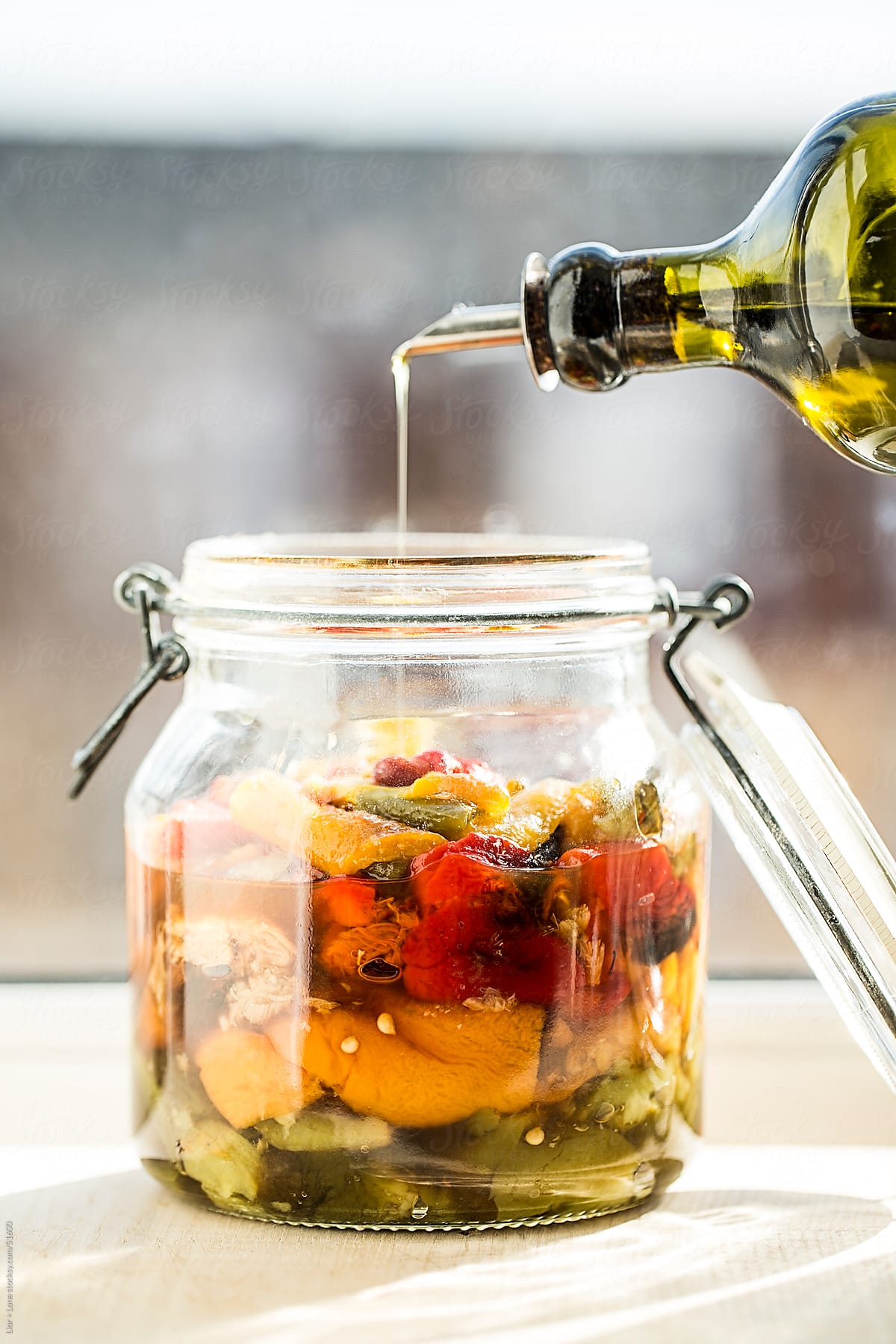 Olive oil pouring into jar of pickled peppers