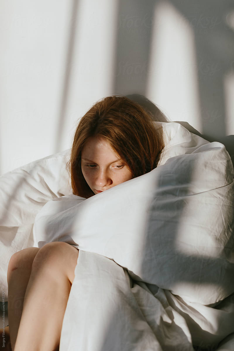 Tired woman sitting under blanket on bed -\
influenza