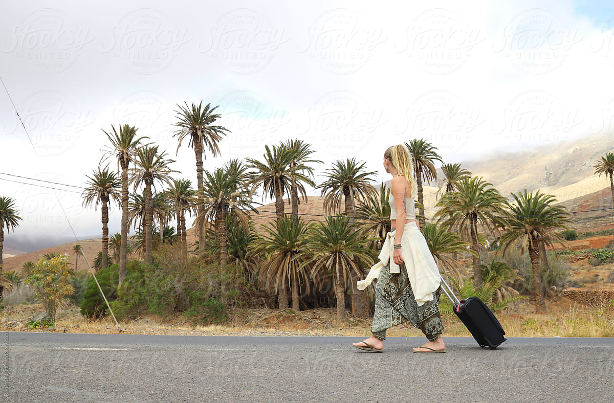 young woman walking on road with suitcase