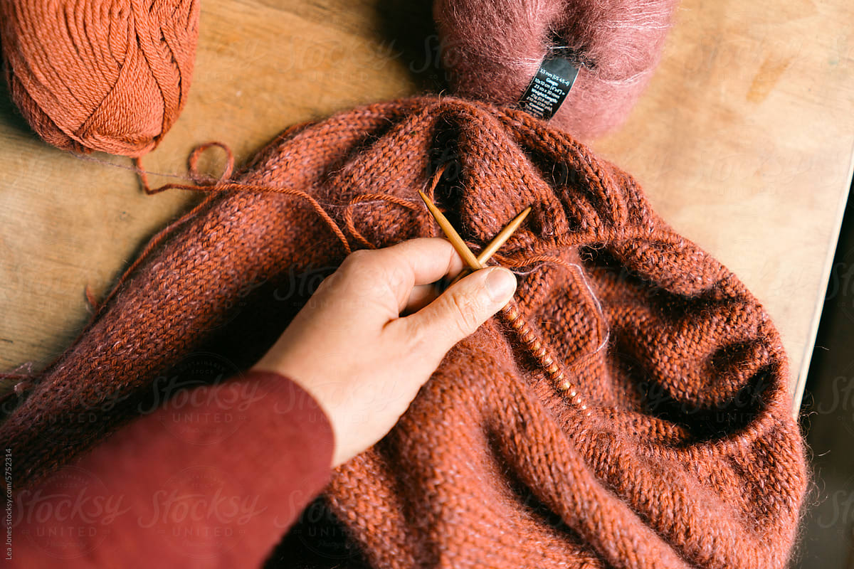 hand holding pink and rusty knitting