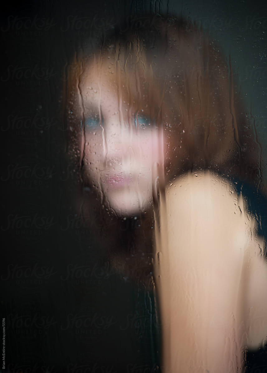 Moody scene of woman looking through rainy window