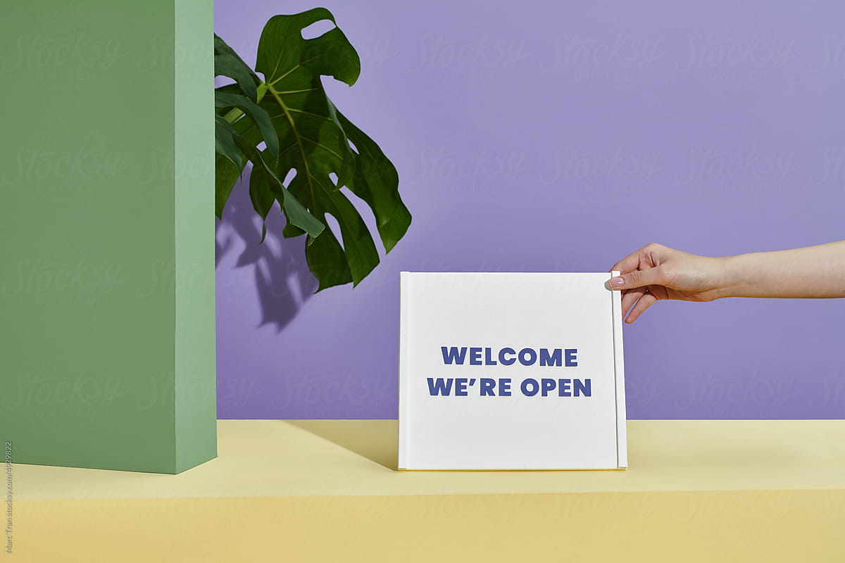 Welcome We\'re open sign on white board with potted plant
