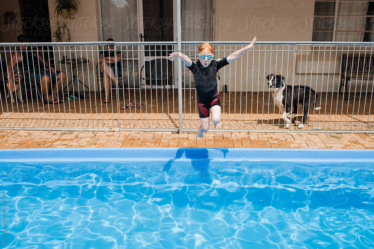 The family dog watches on as a young boy jumps into a swimming pool for fun on a hot day