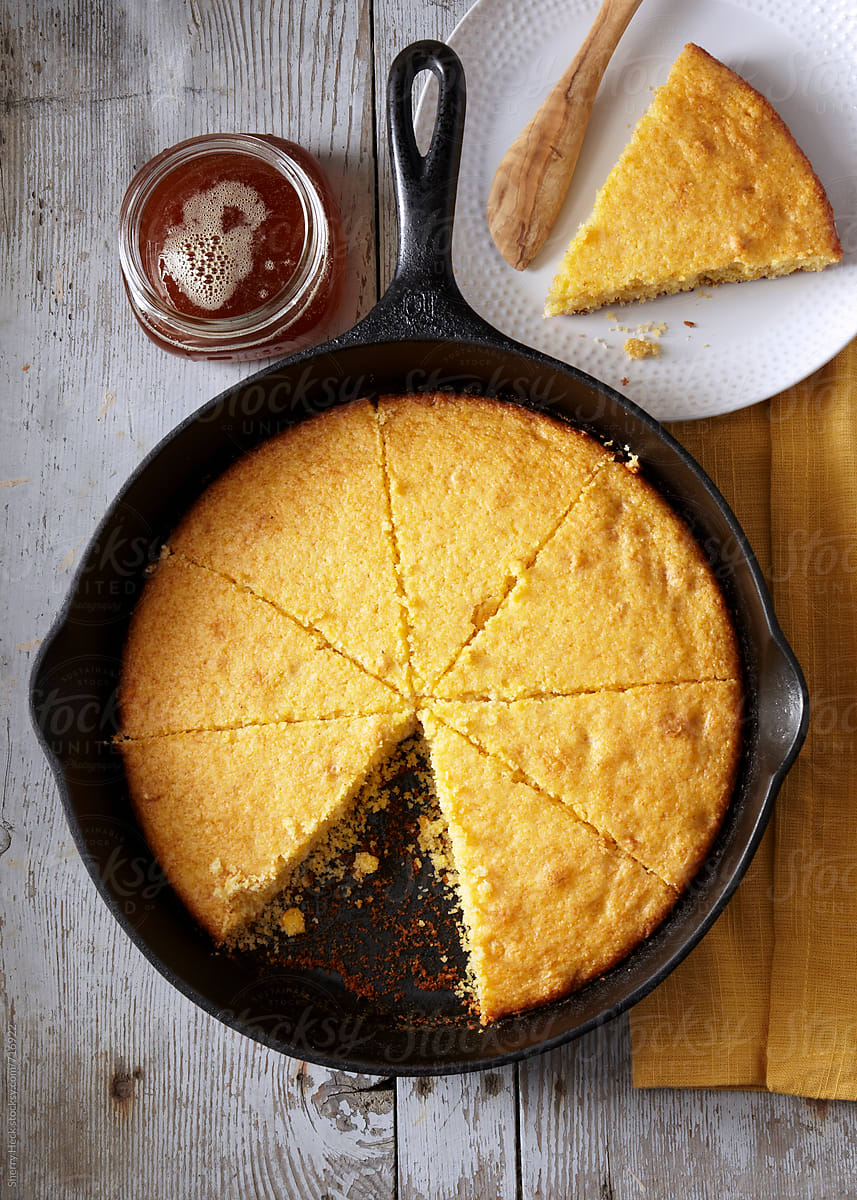 Cornbread in iron skillet cut into pie wedges overhead with honey