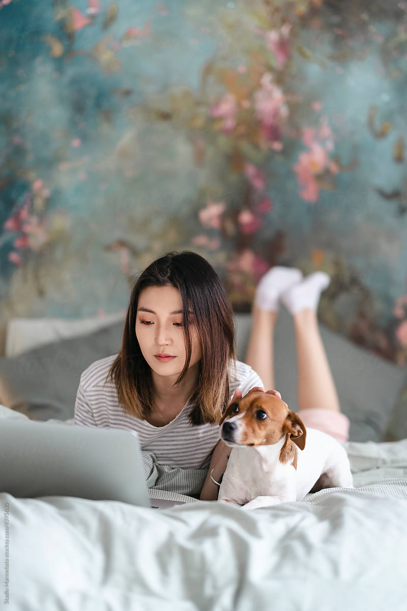 Asian woman using laptop and stroking dog