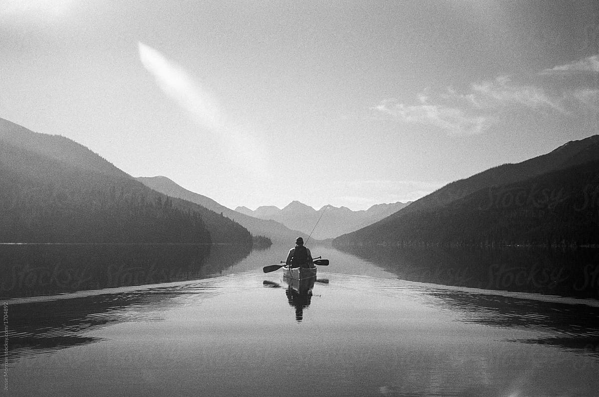 Adult paddling canoe in middle of serene lake BC Canada Bowron Lakes Park