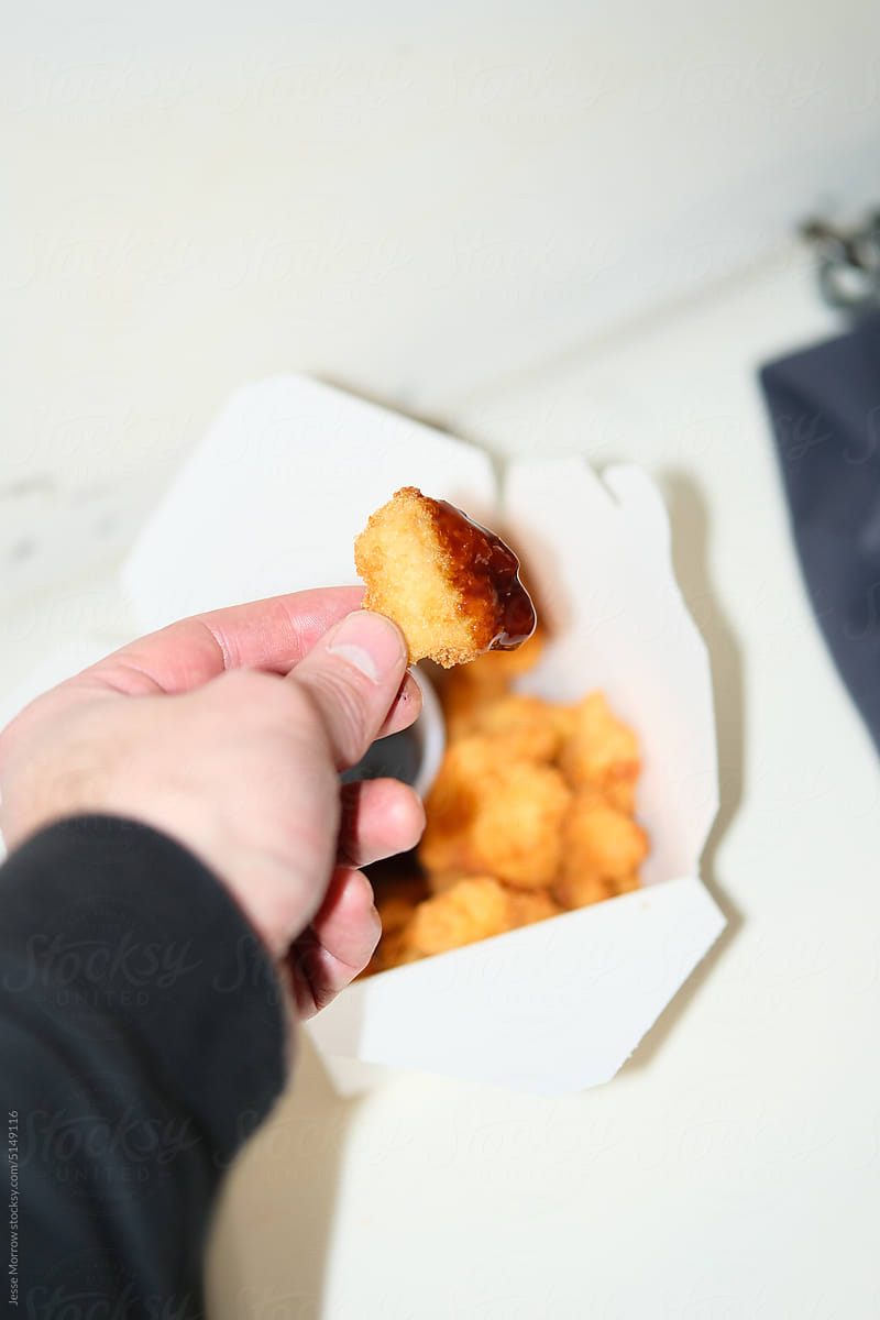 male hand reaching to dip chicken nugget in sauce