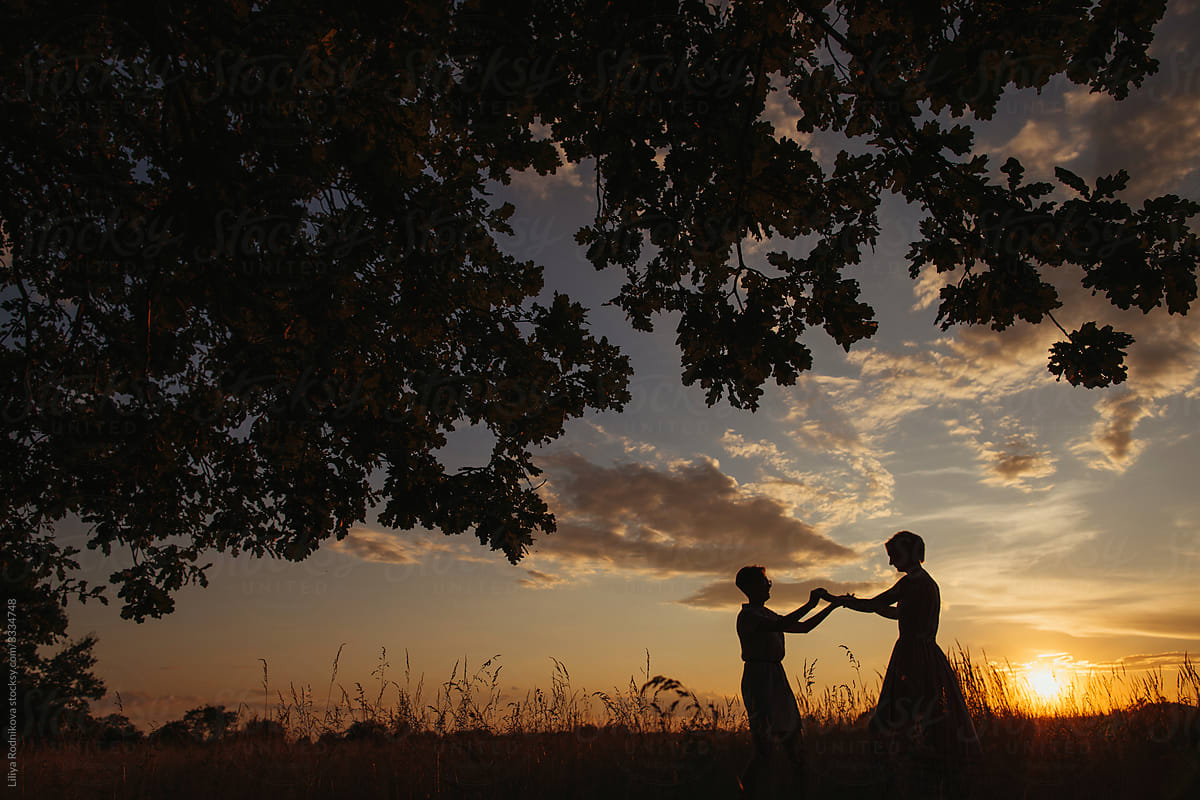 Silhouette of two women dancing against sunset sky
