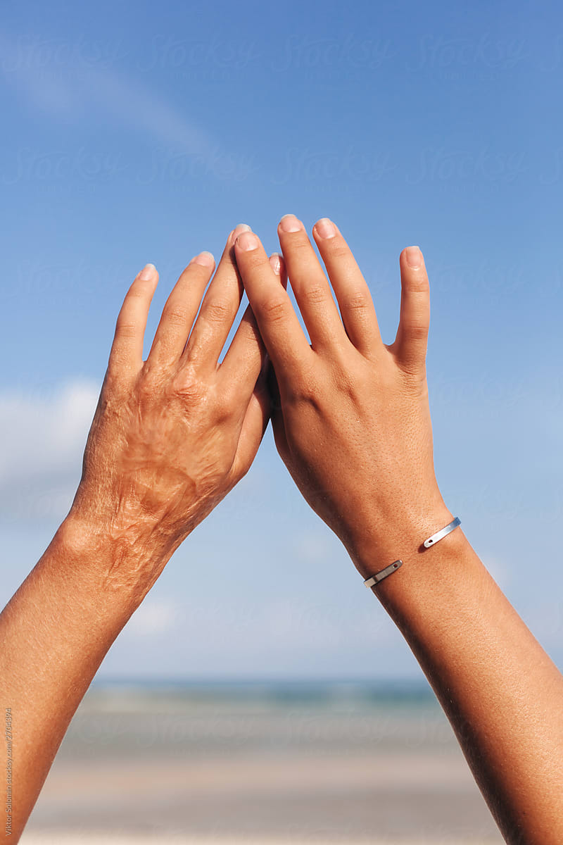 Closeup of young woman tanned hands up on blue summer sky and sea background.