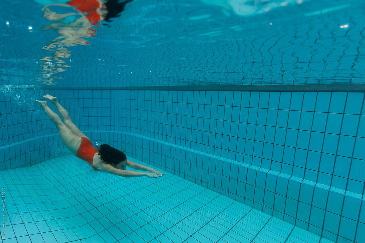 A woman in a red swimsuit is diving underwater in a residential swimming pool