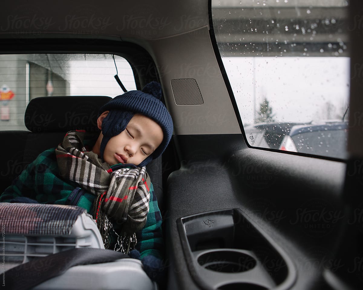 Young child wearing a seatbelt in car booster seat falls asleep during a road trip