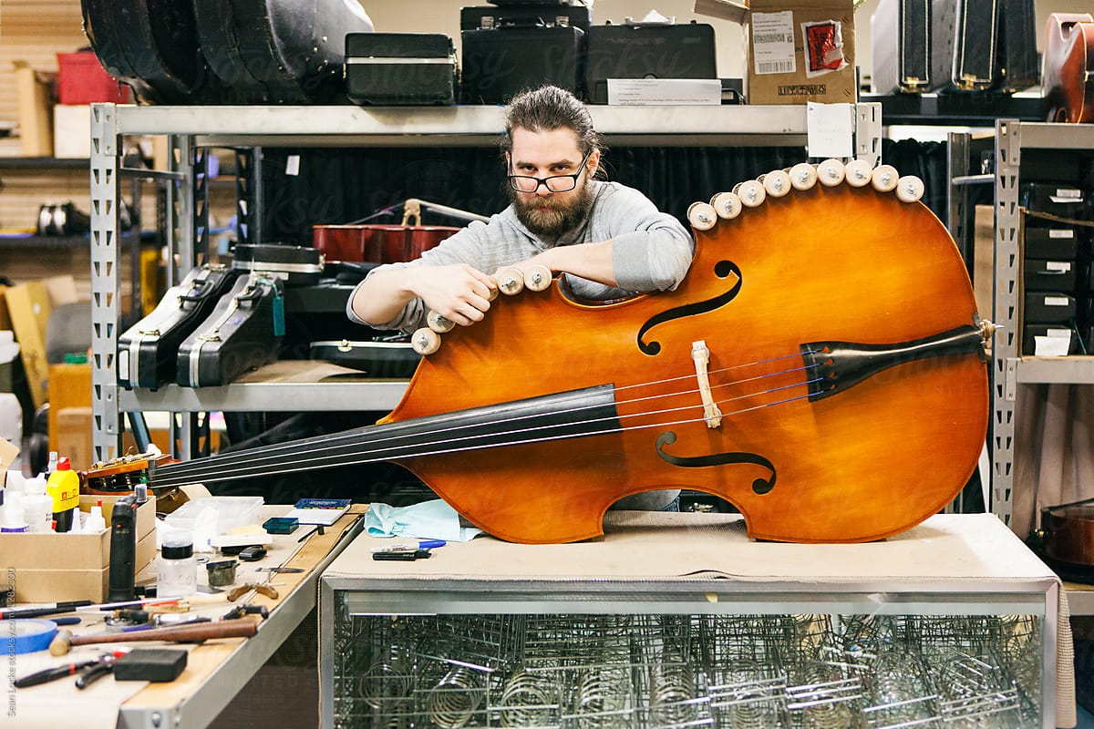 Band: Serious Repairman Looks At Camera With Orchestra Bass