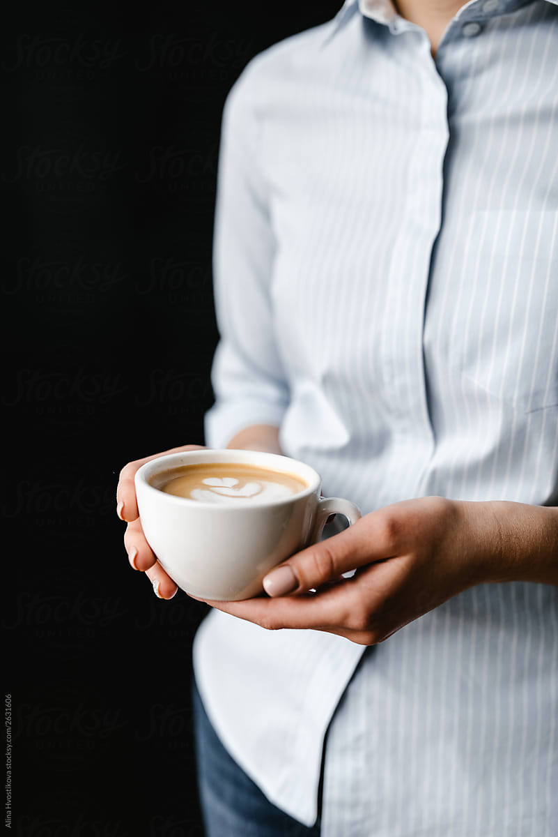 Female holding cup of tasty cappuccino with foam in hands.
