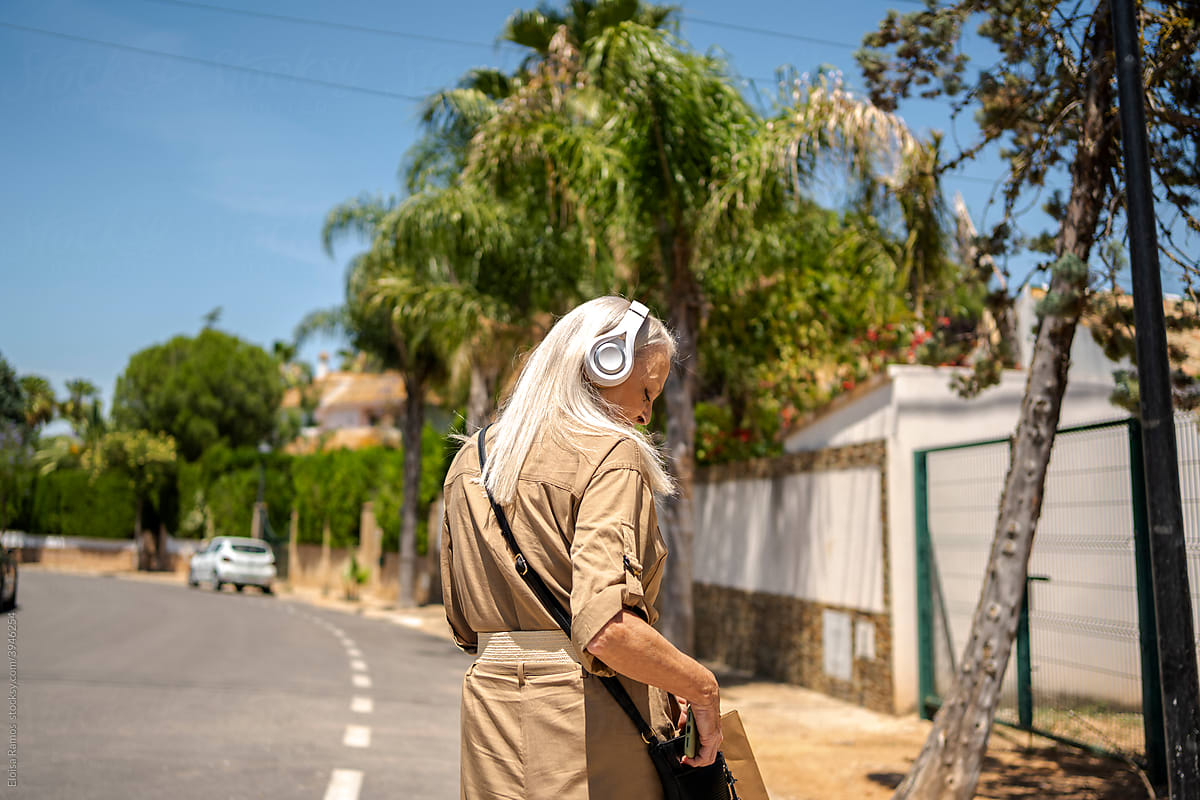Modern senior woman walking down street listening music