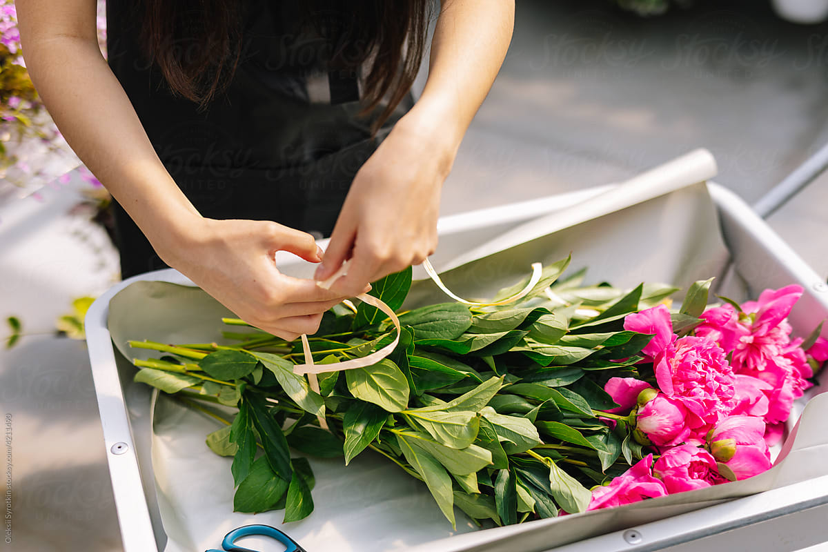Incognito gardener tying cut peonies for create bouquet