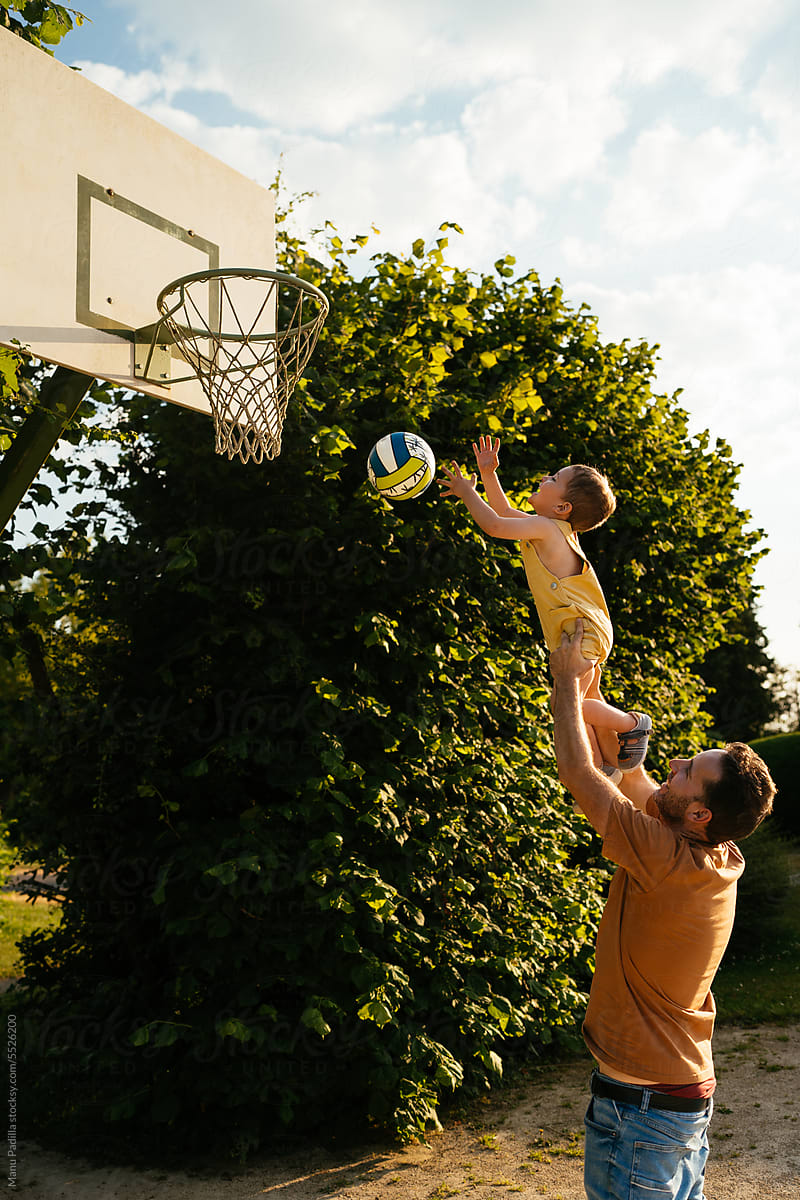 Father and son playing volleyball near hoop in daylight