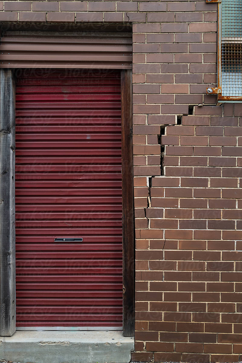 Broken brick wall with red shutter door
