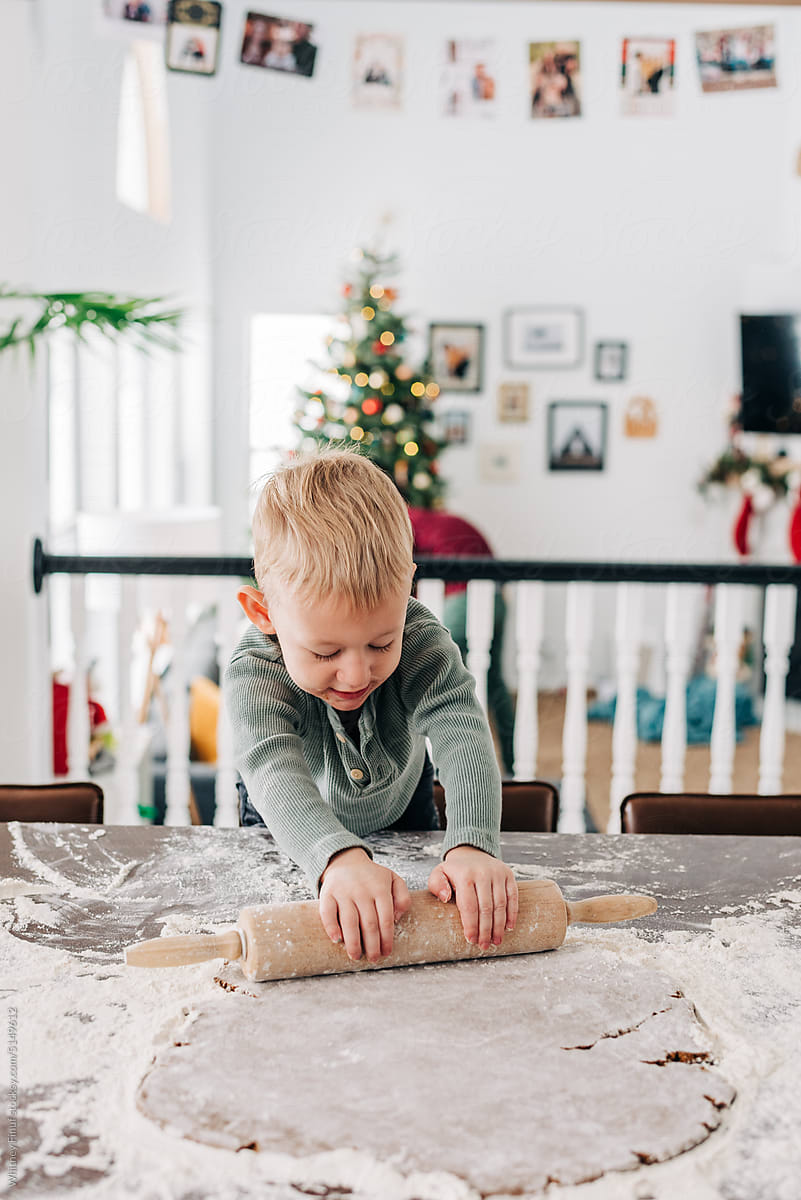 A toddler boy rolls out gingerbread dough in a cozy kitchen