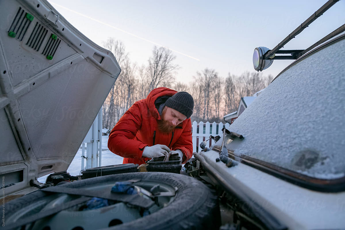 Focused man repairing car engine details in wintertime