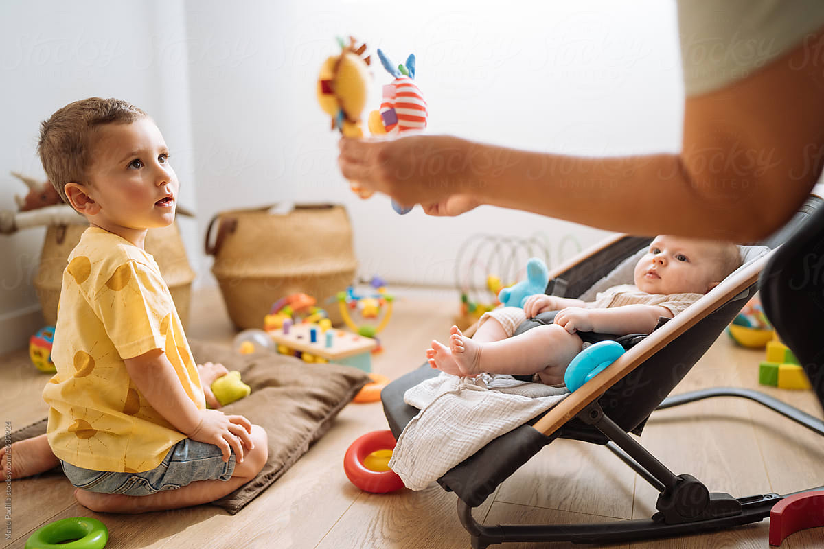 Cute child near baby and anonymous woman showing toys