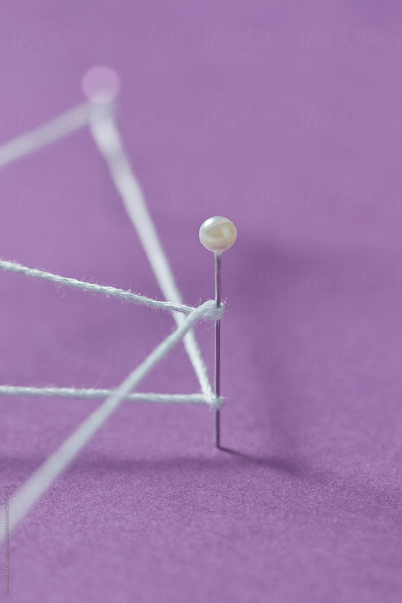 Close up of straight pin stuck in violet paper and wrapped with thread