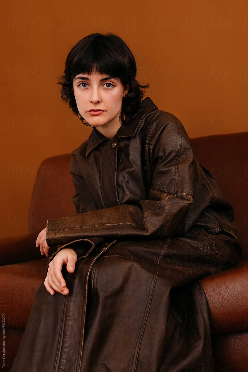 Stylish young lady sitting on brown leather couch