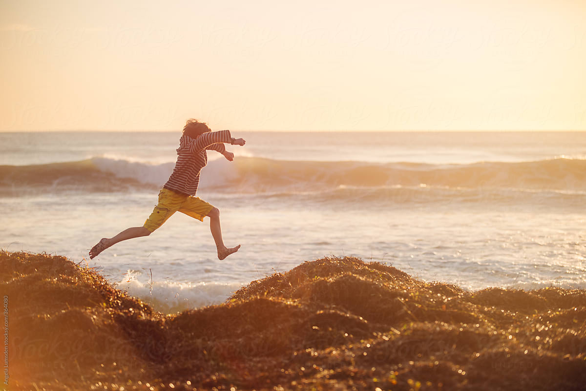 Boy leaping at beach at sunset