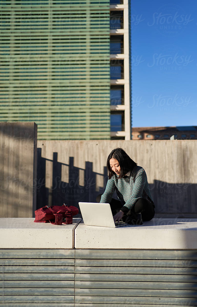 Female student using laptop on street