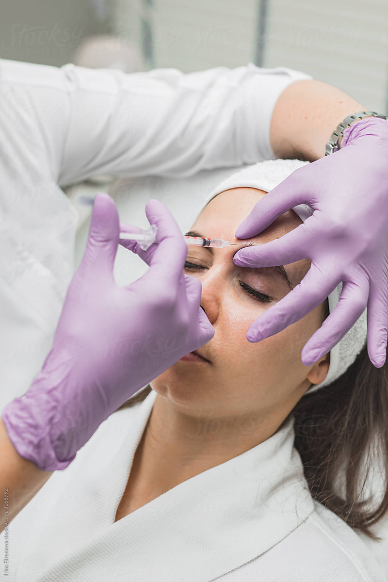 Close up of beautician expert\'s hands injecting botox in female forehead
