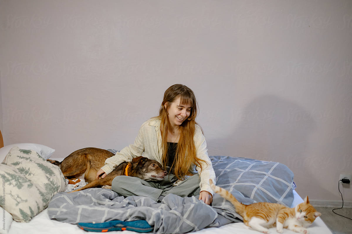 girl with cat and dog sitting on bed