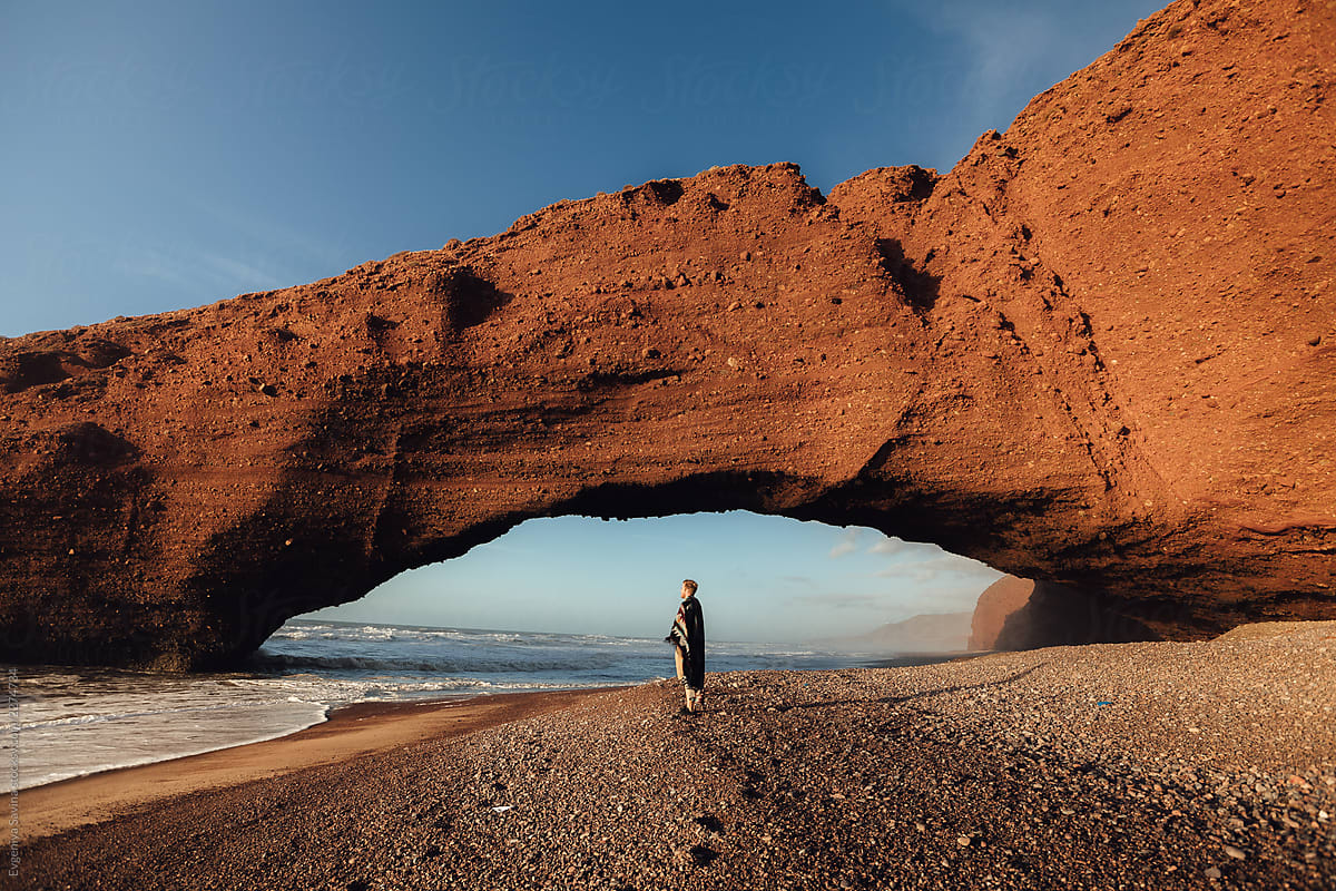 A natural rock arch nearby the ocean and a man walking towards it