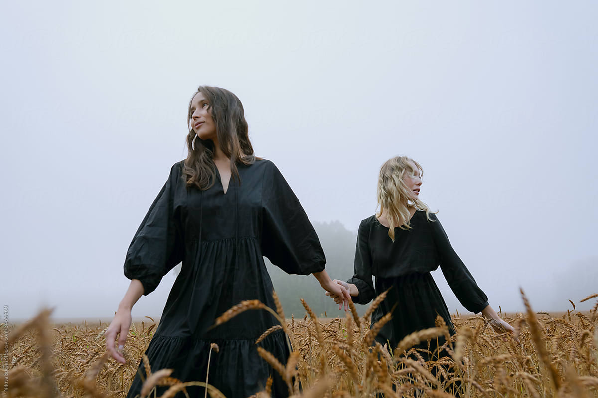 two beautiful girls in black dresses posing in a wheat field