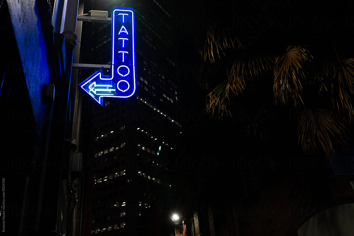Blue neon Tattoo Parlour in dark alley at night
