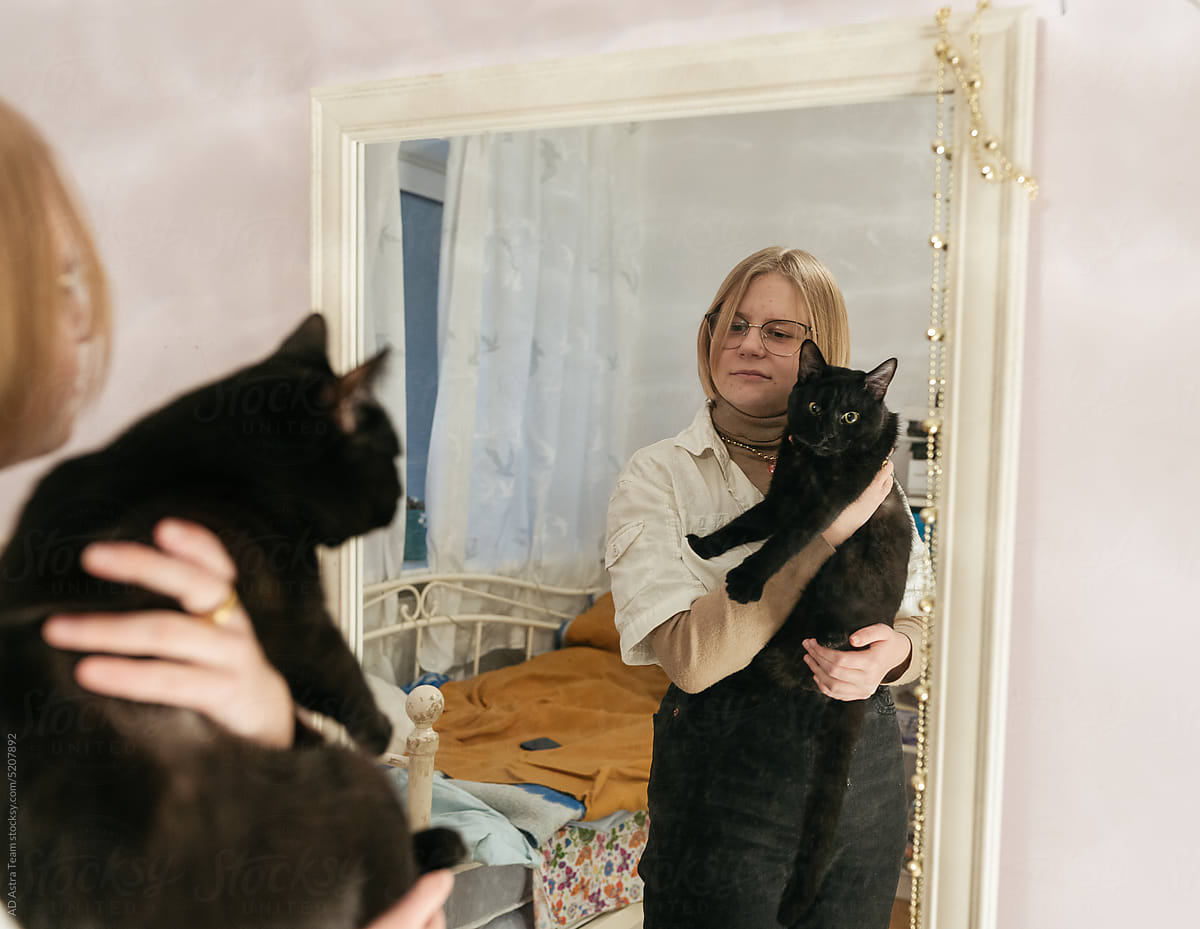 Teenager girl holding a cat and looking into a mirror