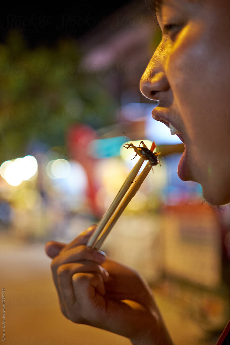 Chinese tourist eating a cricket at a night market in Cambodia