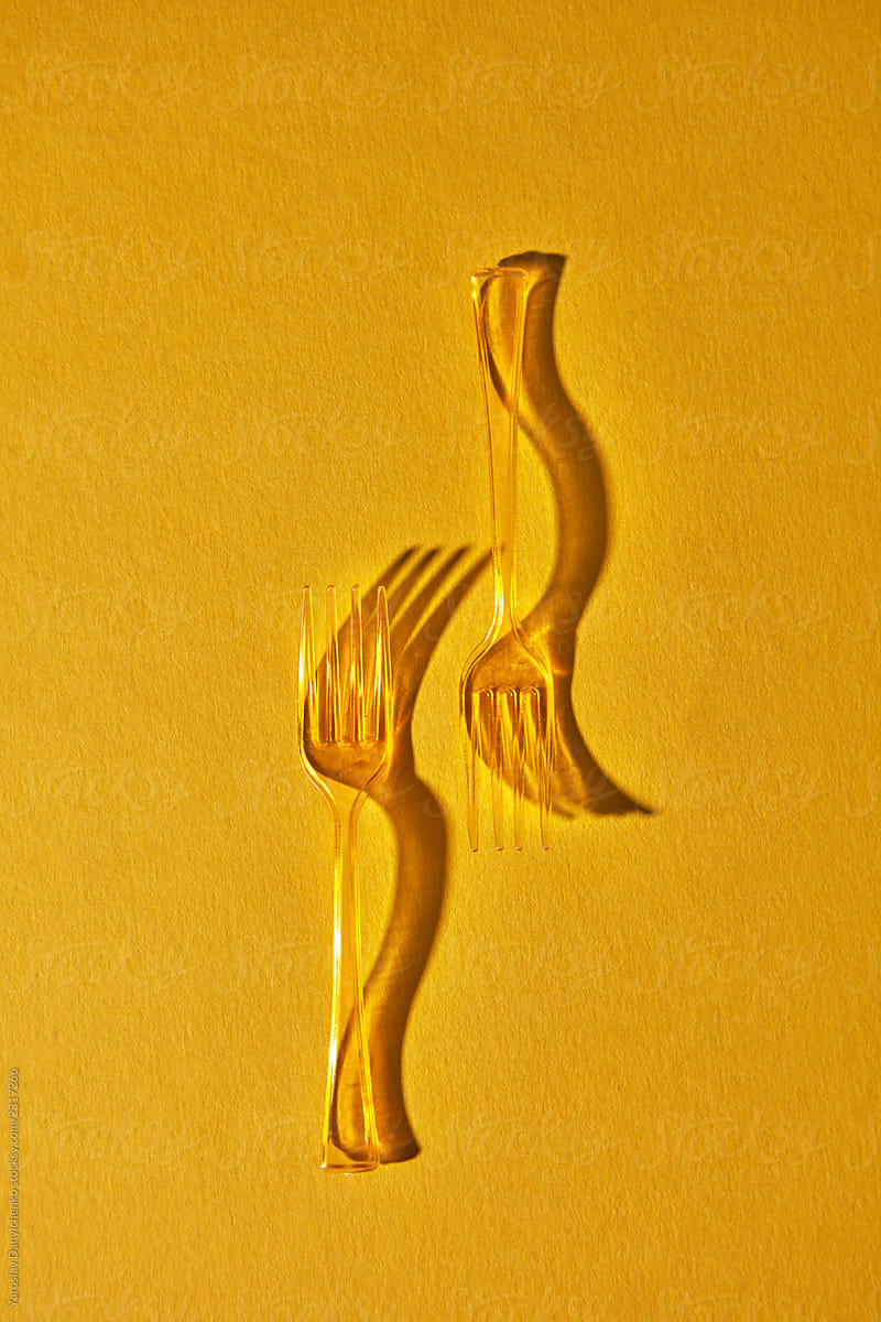 Composition of transparent plastic forks with a pattern of shadows on a yellow background with copy space. Flat lay